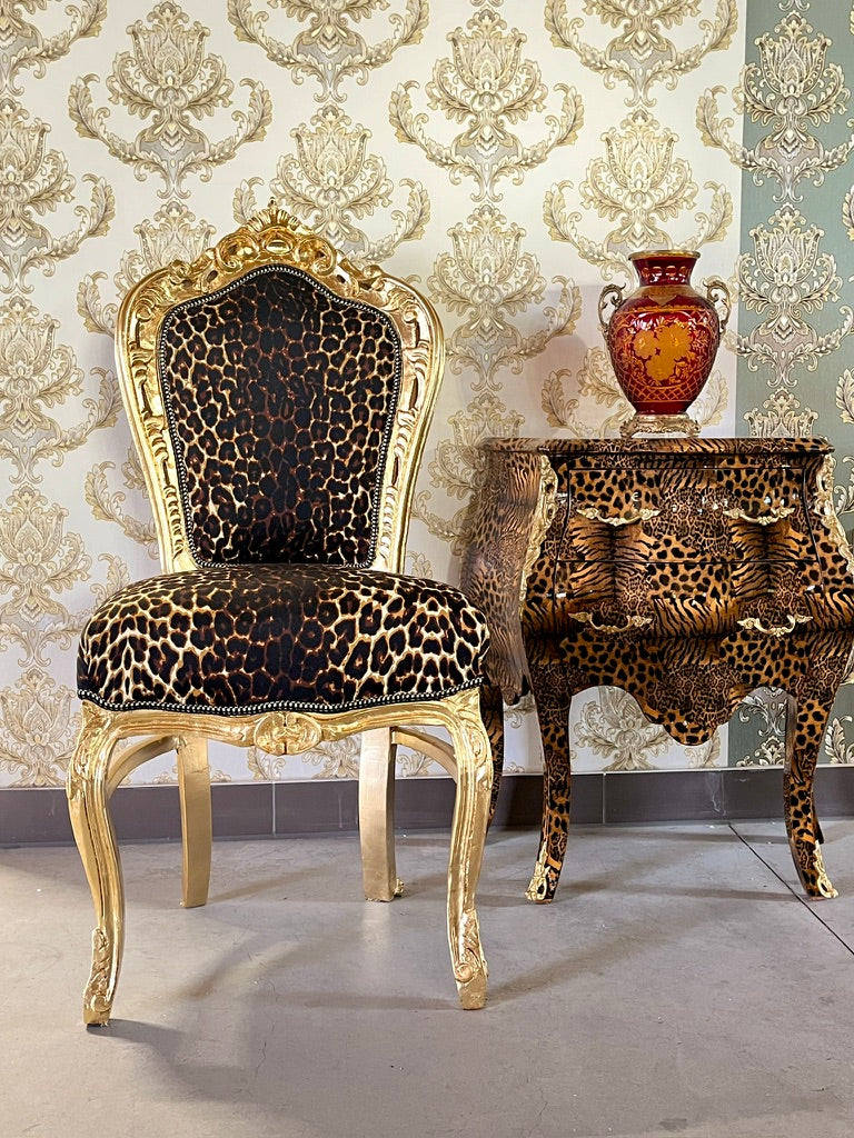 An ornate baroque-style chair with leopard-print upholstery and gold carved legs, positioned next to a matching leopard-print side table against a damask wallpaper background.