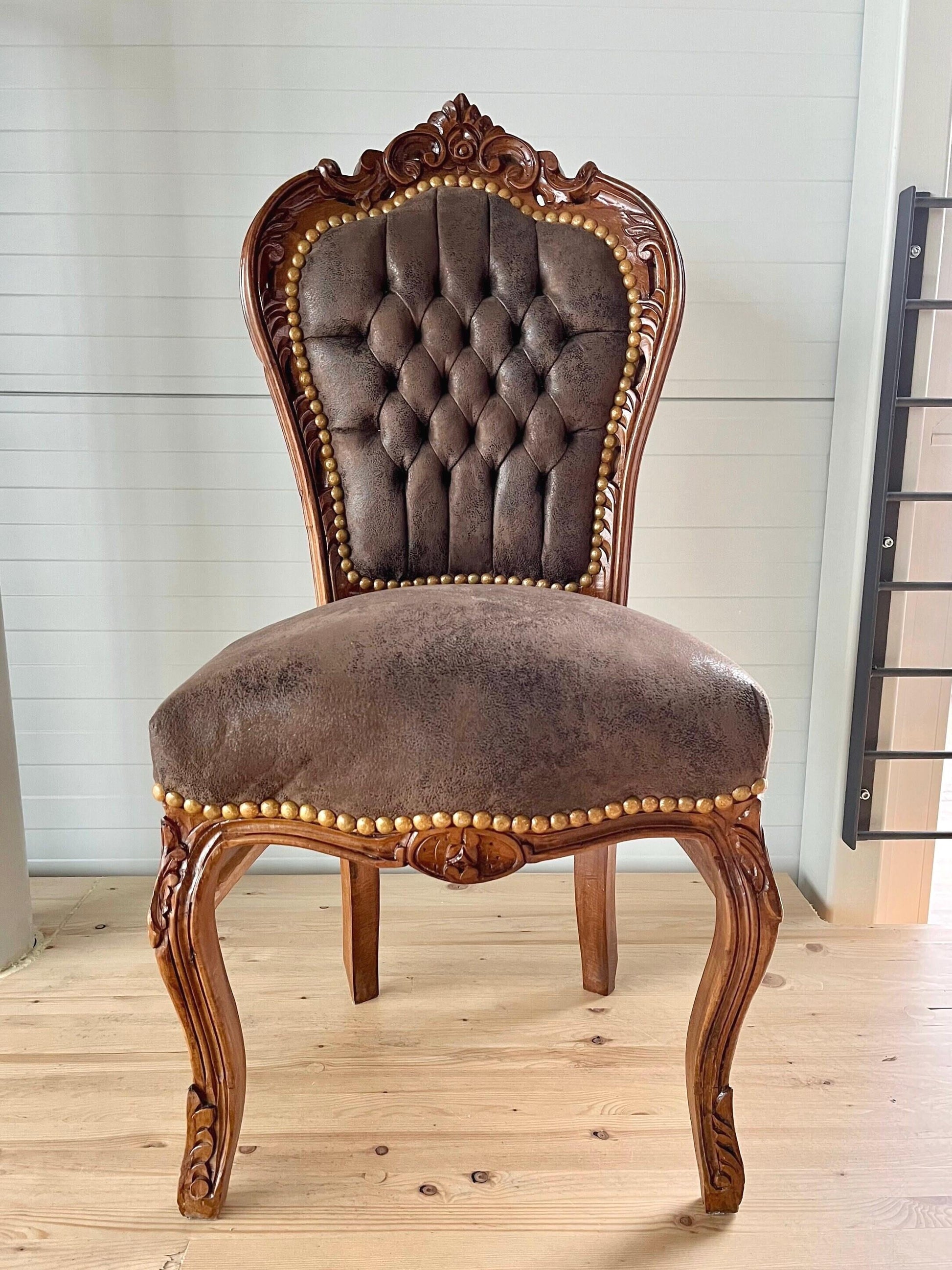 May include: A brown faux suede upholstered chair with a carved wooden frame. The chair has a tufted back and sits on a wooden floor.